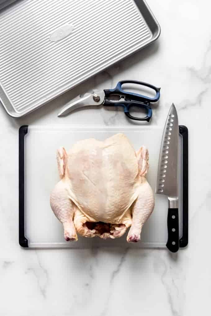 a whole chicken on a cutting board with a large knife and shears to the side