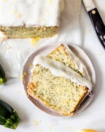 Two slices of lemon poppy seed zucchini bread with lemon glaze on a speckled plate.