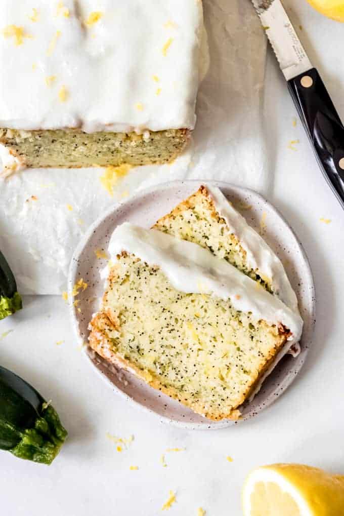 Two slices of lemon poppy seed zucchini bread with lemon glaze on a speckled plate.