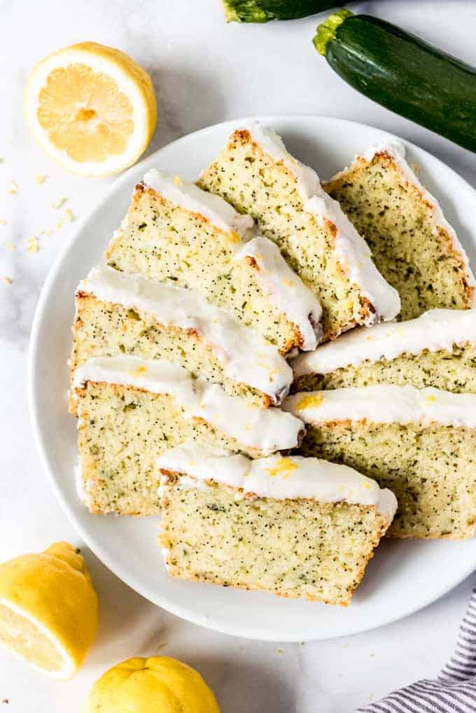Slices of lemon poppy seed zucchini bread topped with glaze arranged on a white plate next to lemon halves.