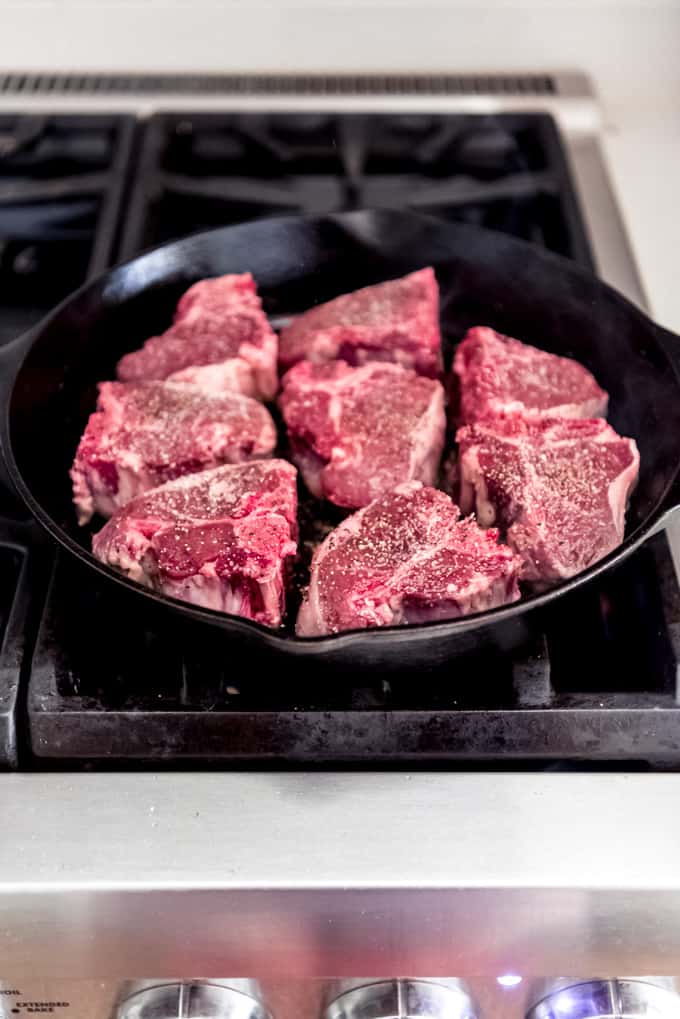 A skillet on the stove filled with seasoned lamb chops