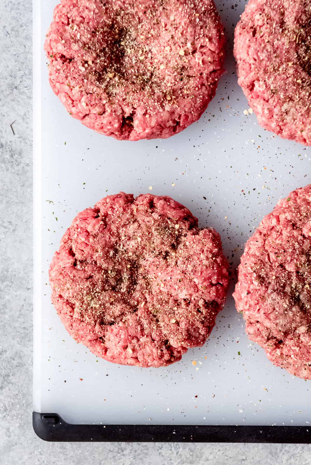 Seasoned hamburger patties on a cutting board.