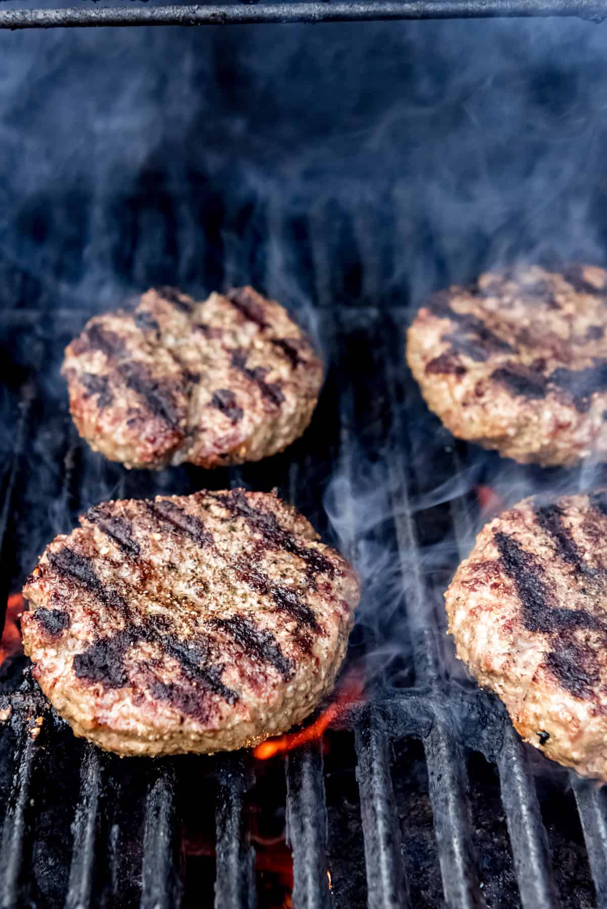 Burgers with grill marks on a grill over flames with smoke.