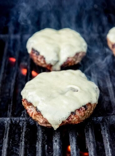 Burgers with cheese on a grill over flames.