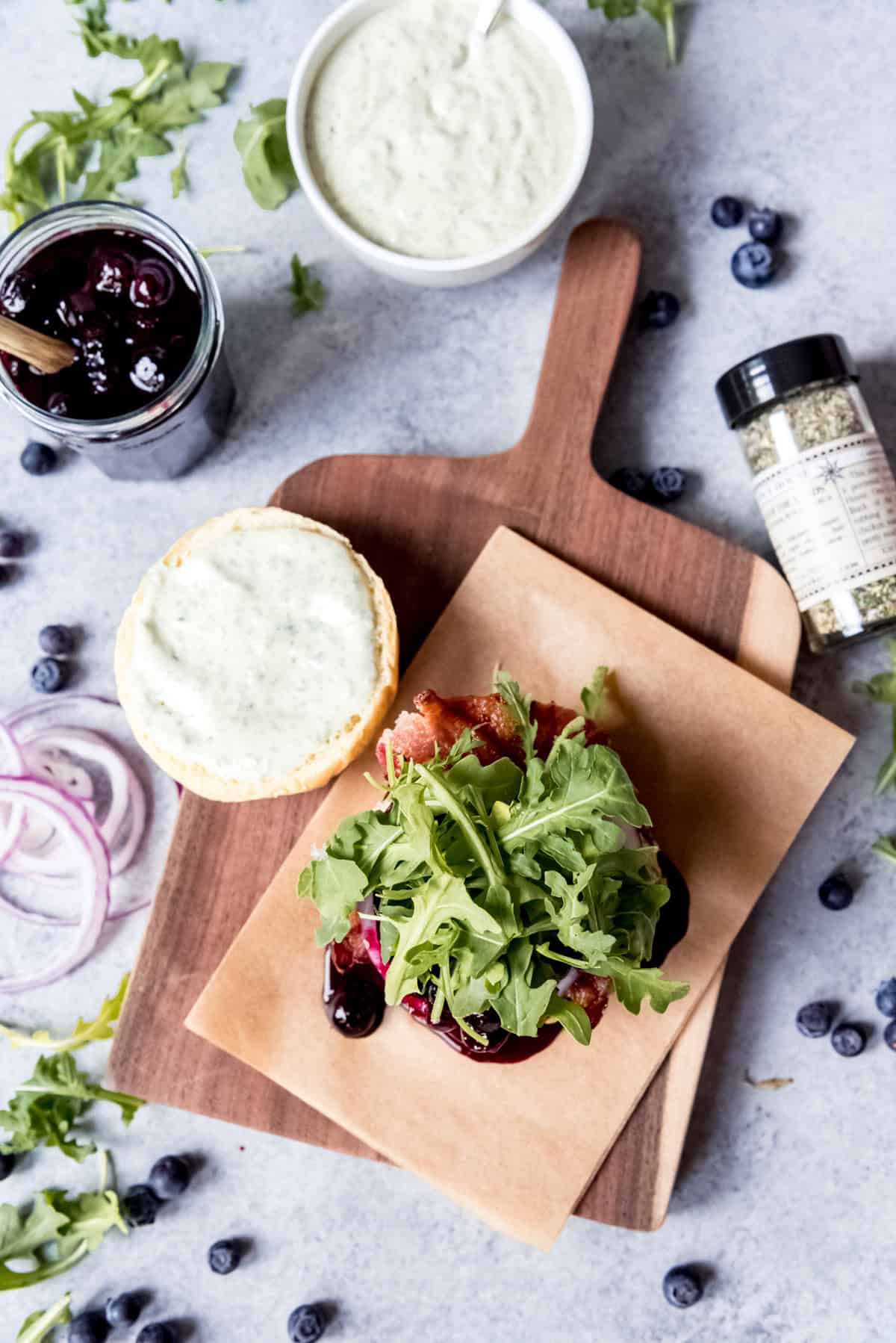 An image of a blueberry bacon burger being assembled on a cutting board.