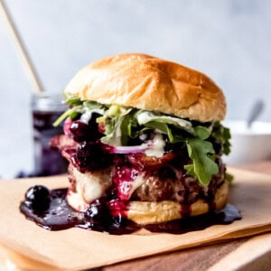 A Red, White, and Blueberry Bacon Burger with Basil Aioli on a piece of parchment paper on top of a wooden cutting board