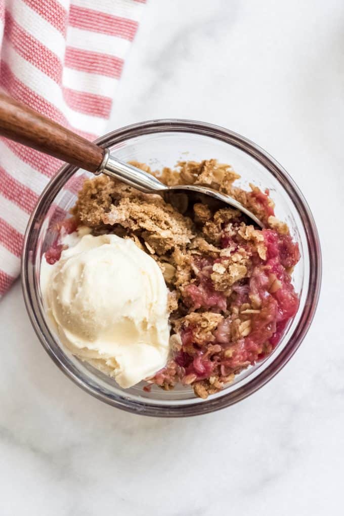 A glass bowl of fruit crisp with a scoop of vanilla ice cream.