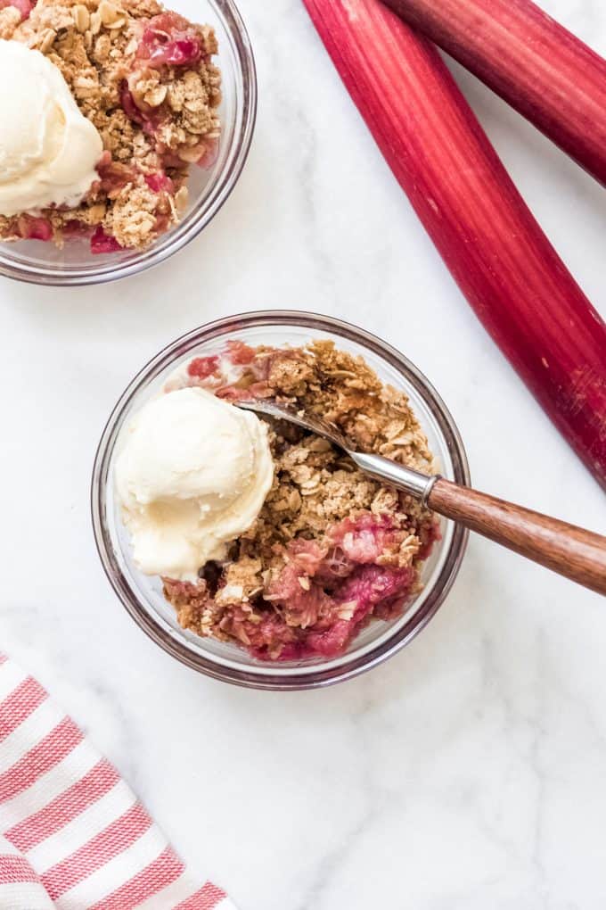 A bowl of rhubarb crisp with a small scoop of vanilla ice cream and a spoon in it.