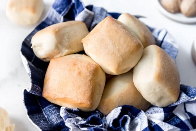 A bowl lined with a blue gingham cloth napkin and filled with homemade rolls.