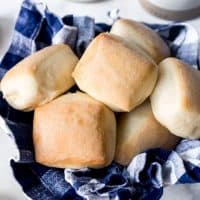 A blue checkered towel in a bowl holding square baked roadhouse copycat rolls inside