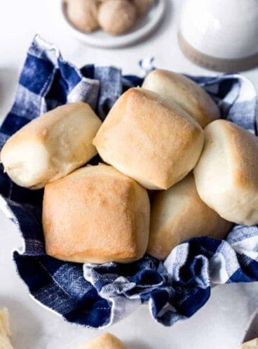 A blue checkered towel in a bowl holding square baked roadhouse copycat rolls inside
