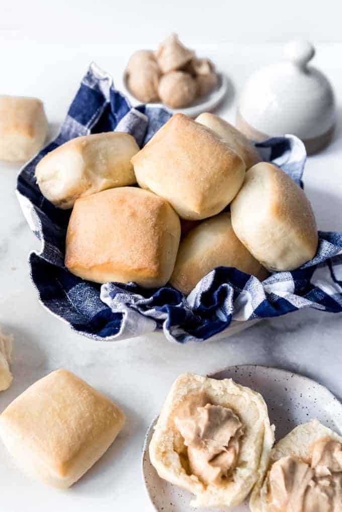A basket full of homemade dinner rolls next to a plate with a roll spread with cinnamon honey butter.