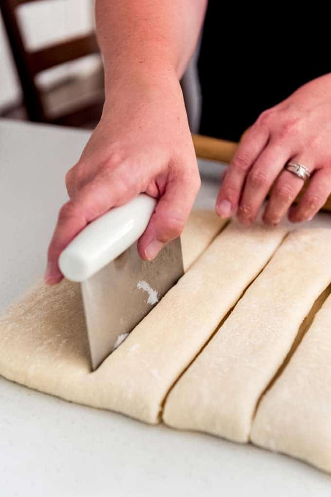 hands cutting dough into long strips using a dough cutter