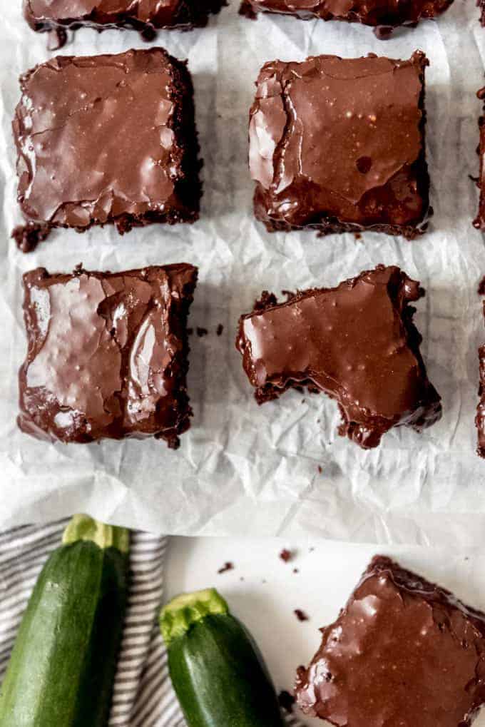 Four zucchini brownies on parchment paper with a bite taken out of one.