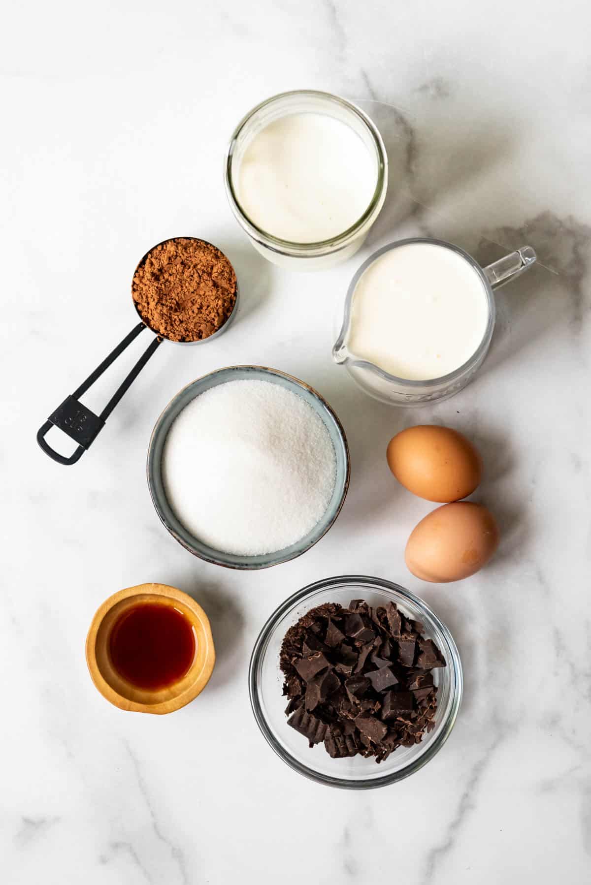 The ingredients for chocolate ice cream separated into individual bowls or containers on a marble surface.