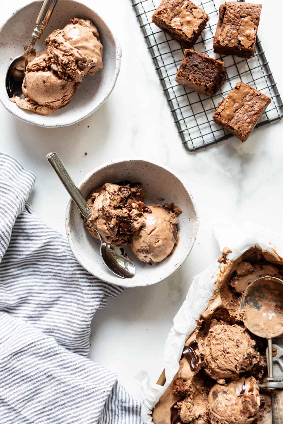 Bowls filled with scoops of chocolate ice cream next to brownies on a wire rack.