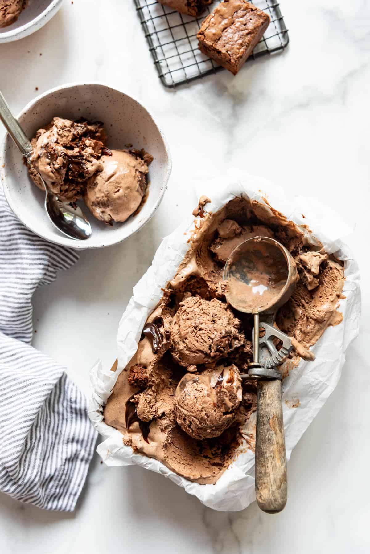 Scoops of chocolate ice cream with a vintage scoop in a pan of homemade ice cream next to a bowl of more ice cream.