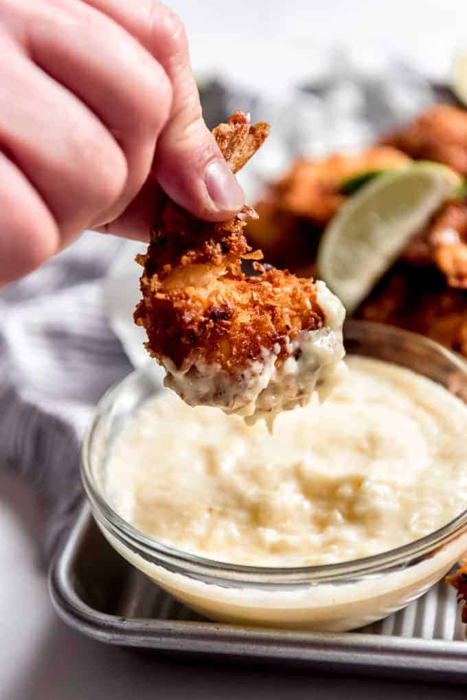 A hand lifting a coconut shrimp out of a pina colada dipping sauce.