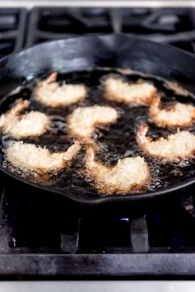 Coconut shrimp frying in oil in a large skillet.