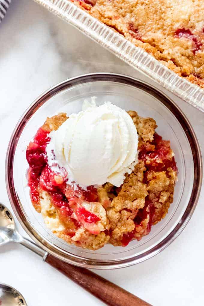 A scoop of vanilla ice cream over cherry pineapple dump cake in a glass bowl.