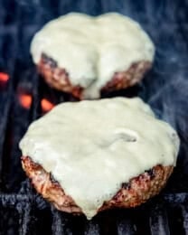 Burgers with cheese on a grill over flames.