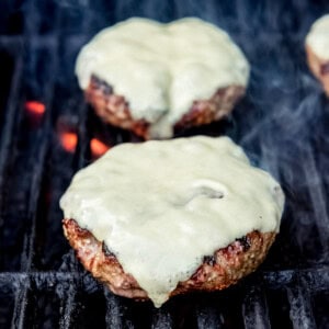 Burgers with cheese on a grill over flames.