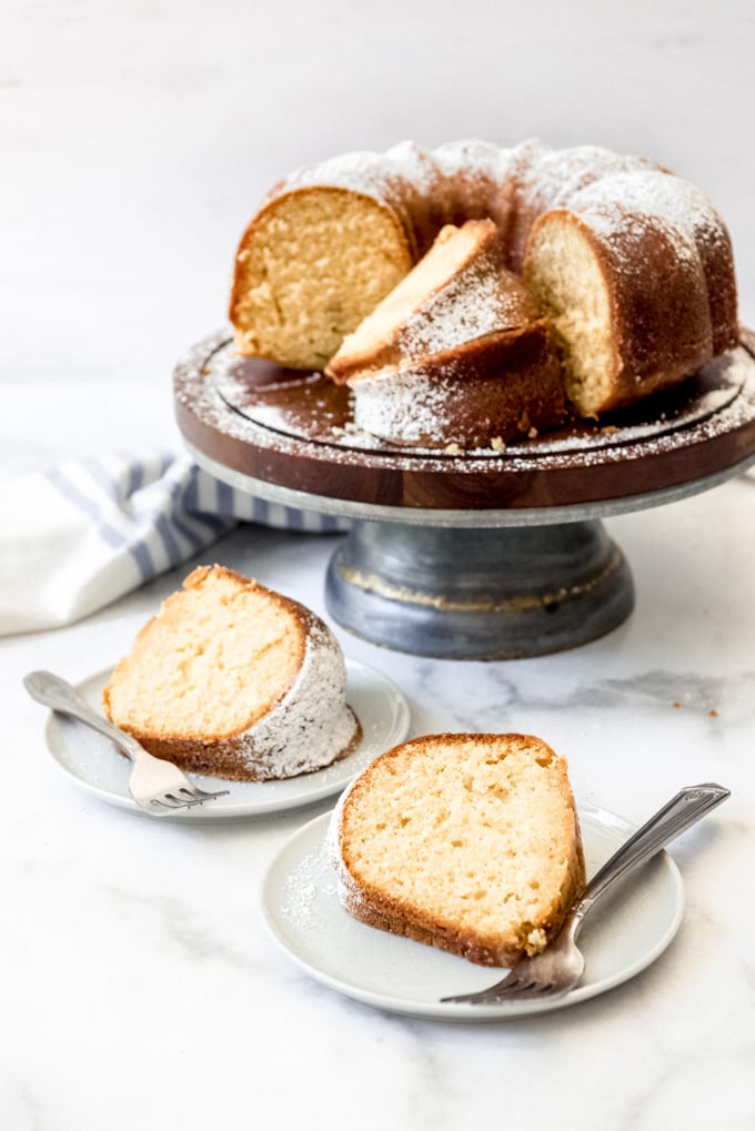 Two slices of bundt cake on plates with forks in front of the cake on a cake stand.