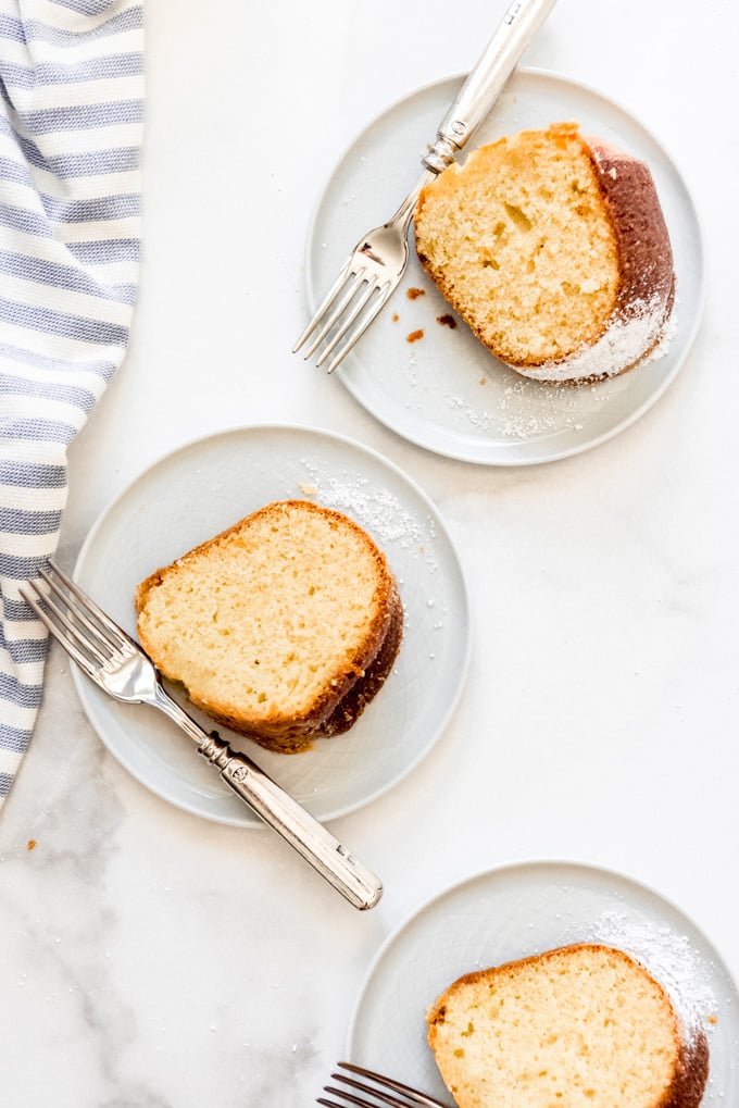 Three slices of vanilla pound cake on white plates with forks.