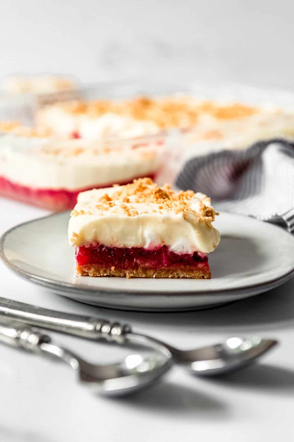 A slice of rhubarb pudding dessert on a plate next to a baking dish with the rest of the dessert.