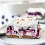 A slice of blueberry delight topped with whipped cream and pecans on a plate.