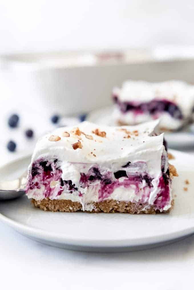A slice of blueberry delight topped with whipped cream and pecans on a plate.