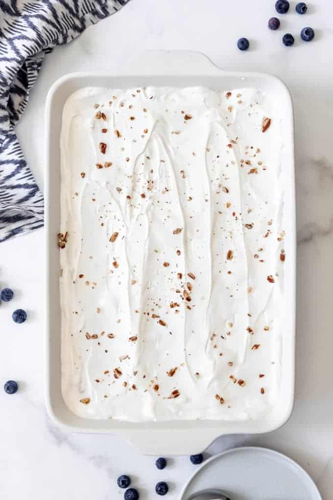 cream mixture and scattered nuts to garnish this blueberry delight in a white baking dish