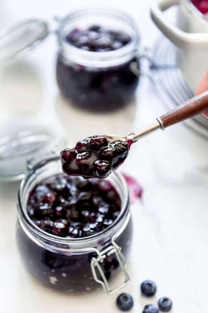 A spoon lifting up a scoop of blueberry pie filling from a jar.