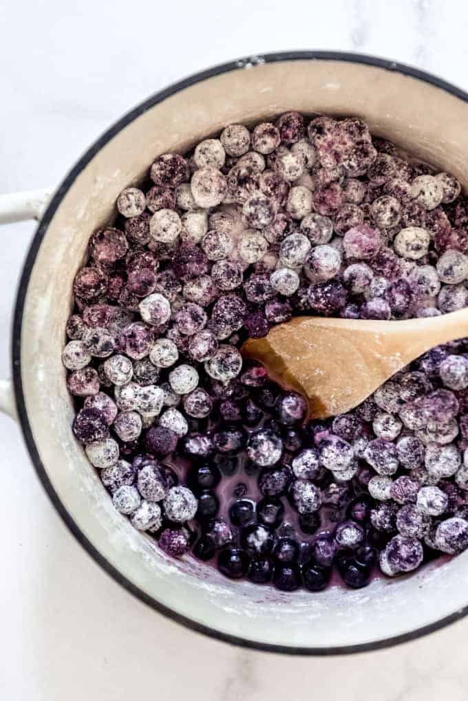 A large pot full of blueberries with sugar and cornstarch with a wooden spoon in it.