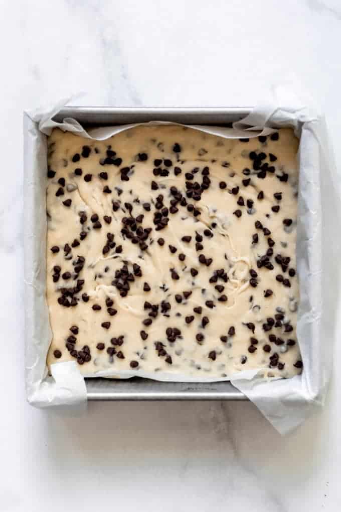 Cookie dough fudge topped with chocolate chips in a pan lined with a parchment paper sling.