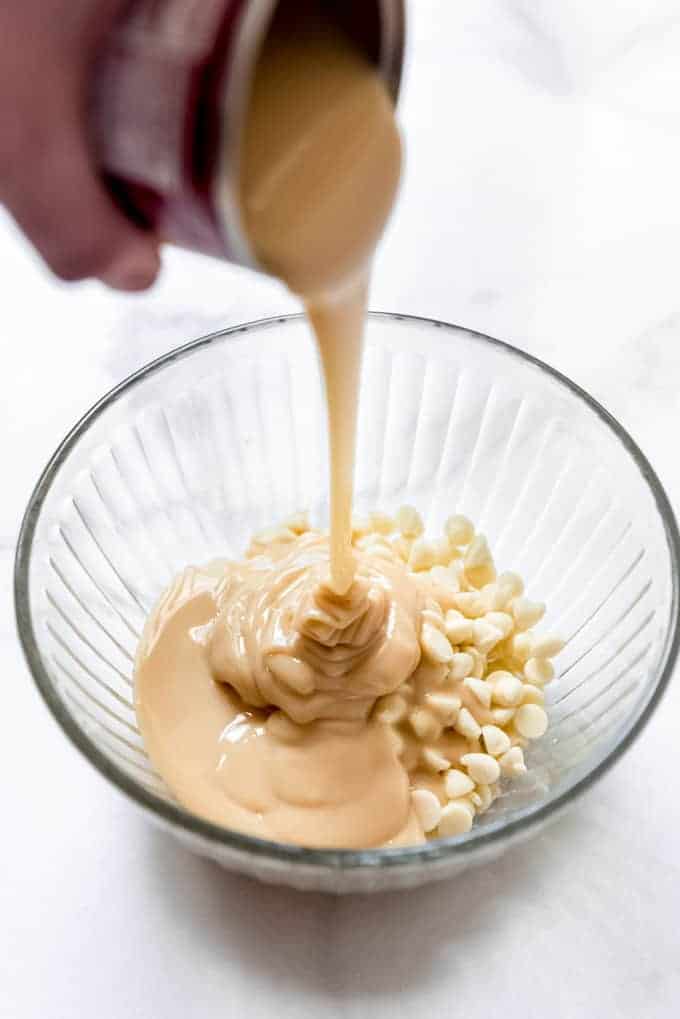 Sweetened condensed milk being poured over white chocolate chips in a bowl.