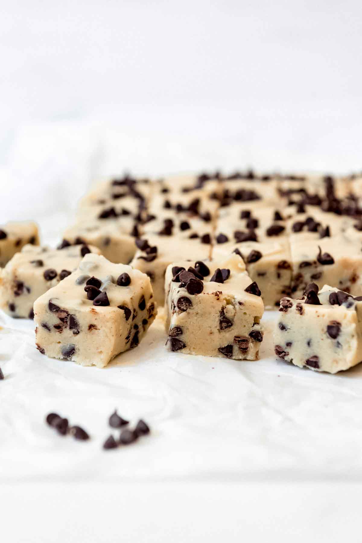 Squares of cookie dough fudge on white parchment paper.