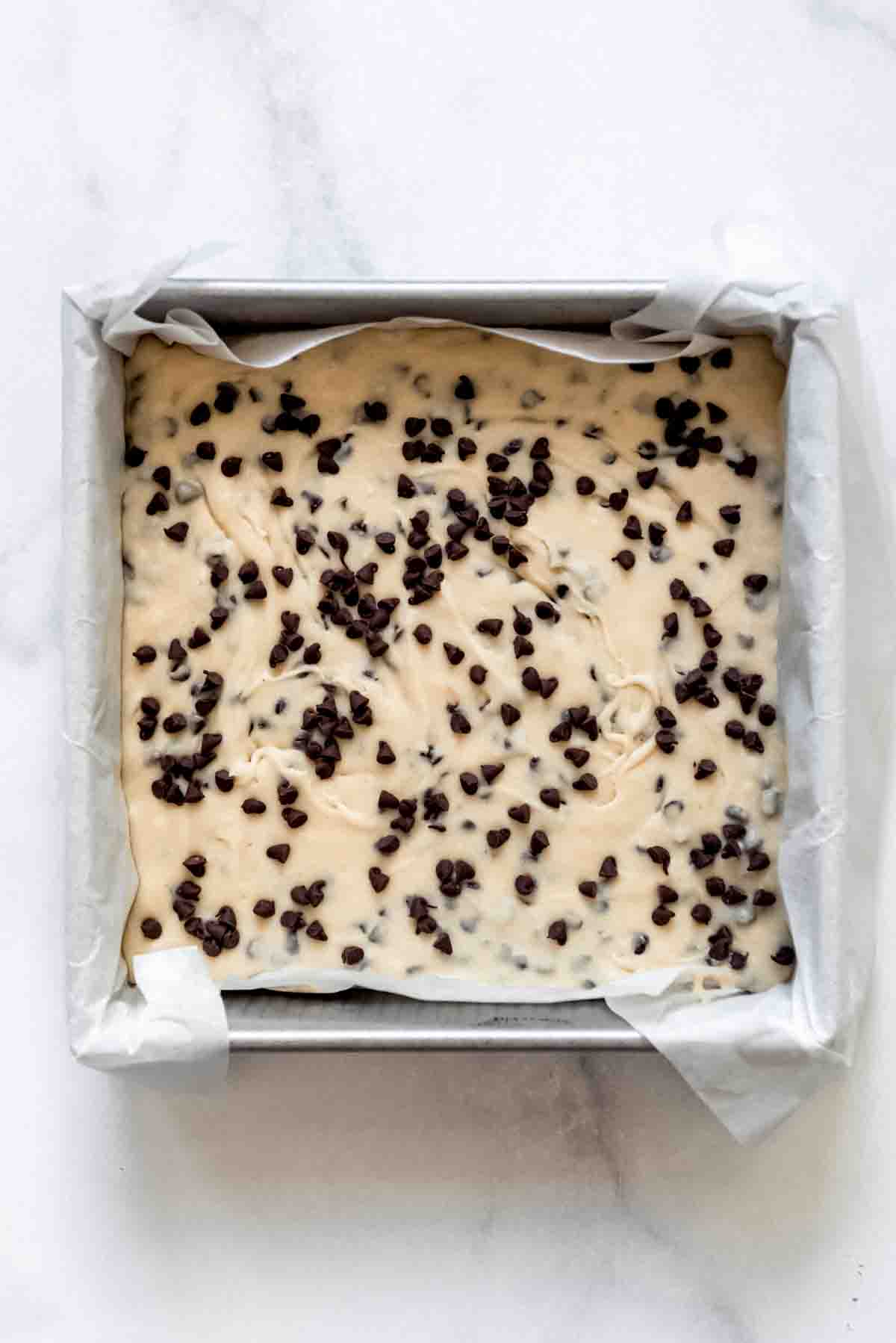 Cookie dough fudge topped with chocolate chips in a pan lined with a parchment paper sling.