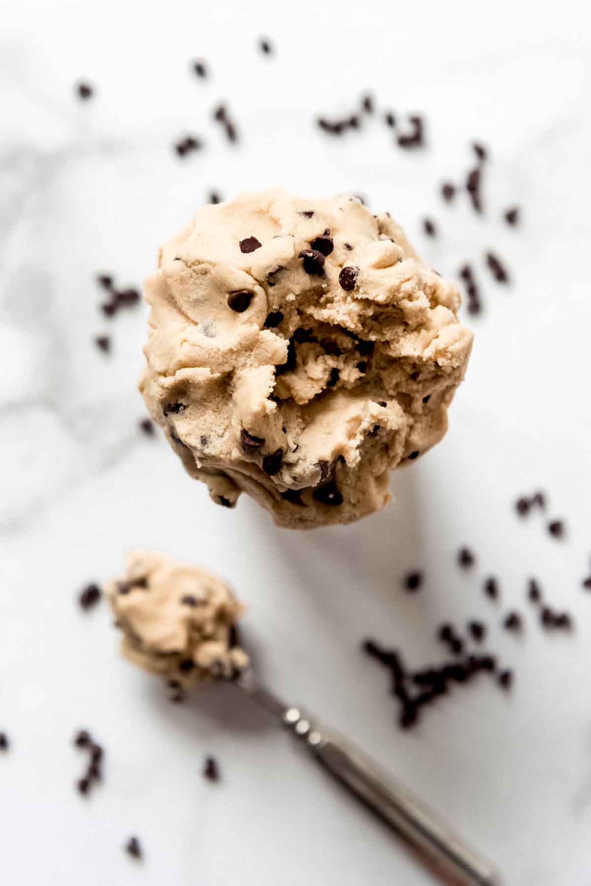 Edible chocolate chip cookie dough in a cup next to a spoonful of dough.