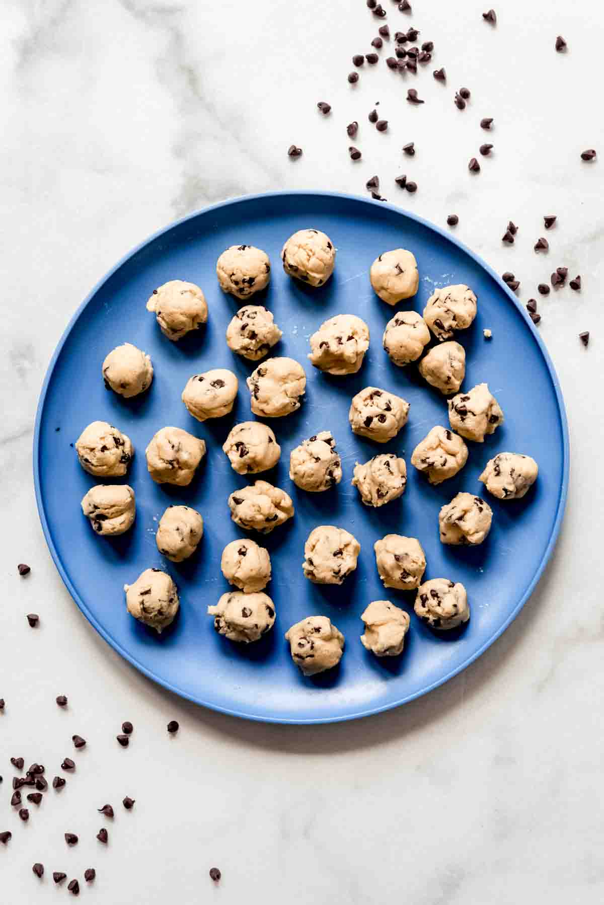 A blue plate with small balls of chocolate chip cookie dough on it.