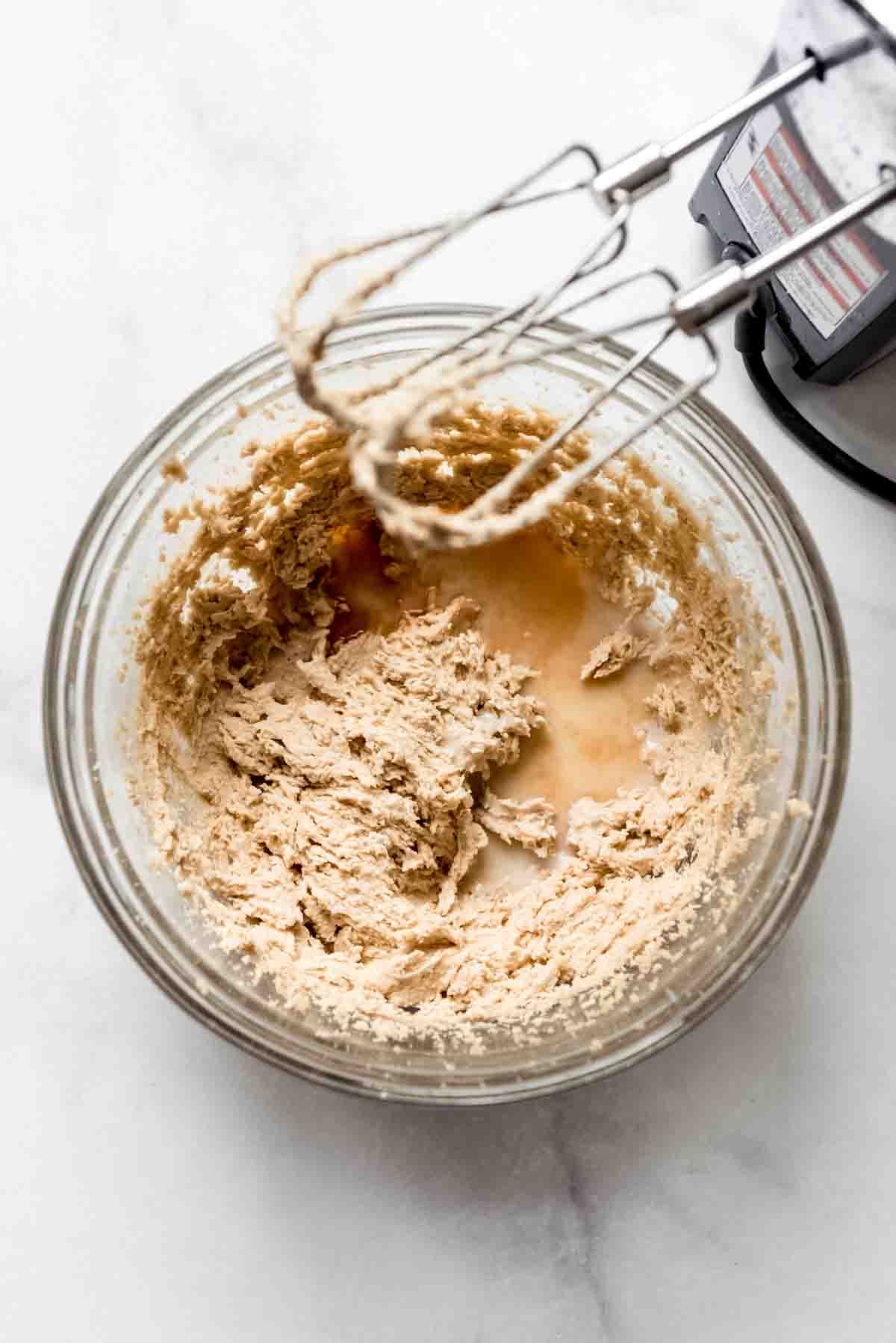 A beaten bowl of sugars and butter with an electric mixer nearby.