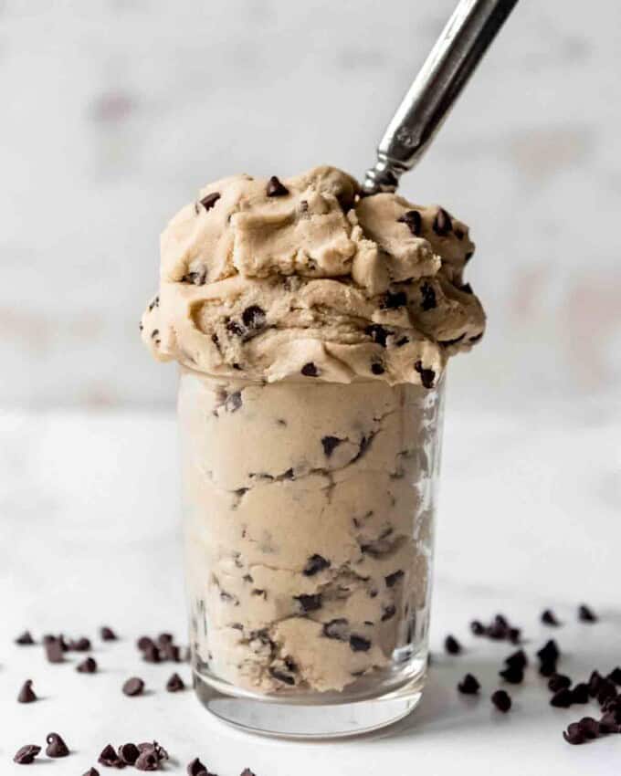 A glass full of eggless chocolate chip cookie dough with a spoon in it.