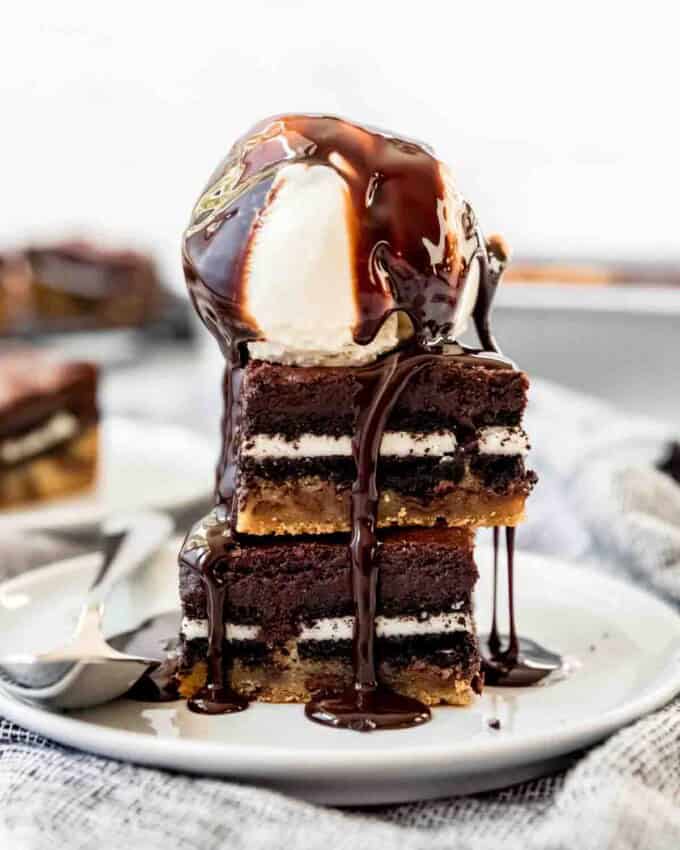 Two slutty brownies stacked on a plate with a scoop of vanilla ice cream on top.