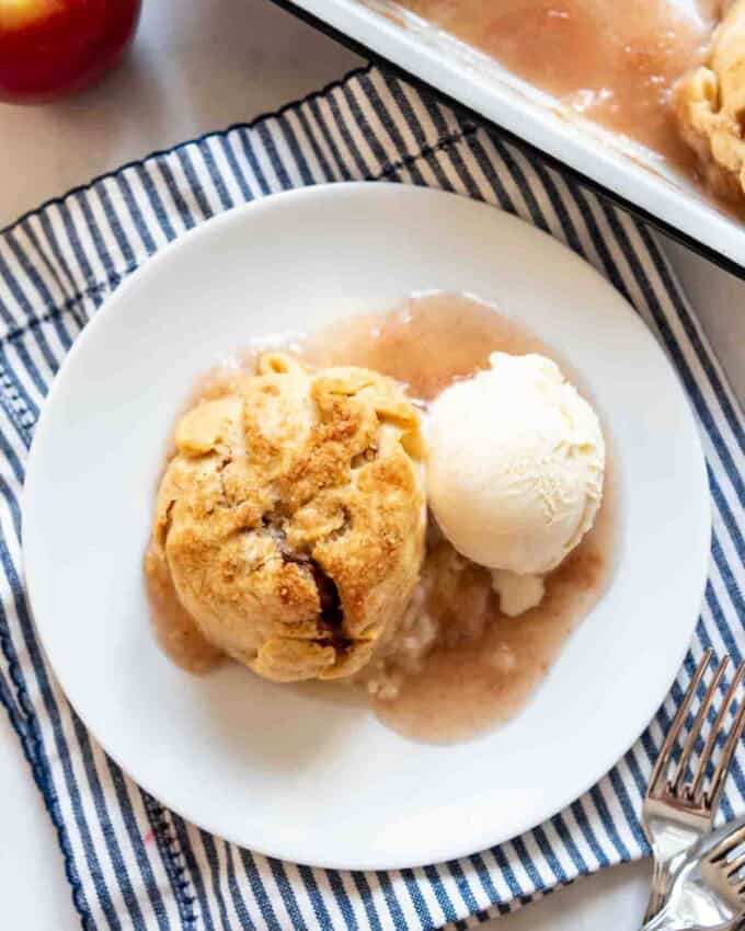 An apple dumpling on a white plate with a scoop of vanilla ice cream.