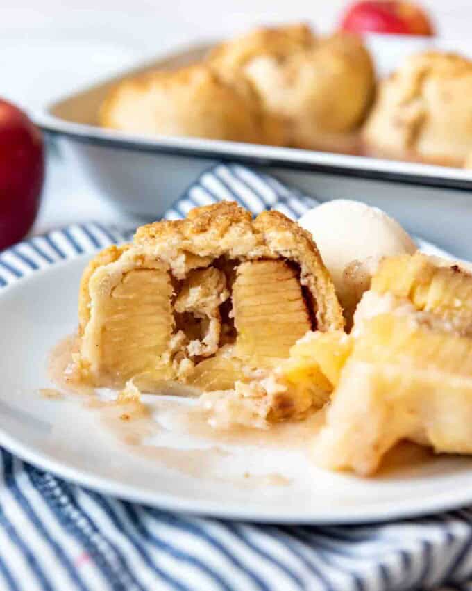 An apple dumpling that has been sliced in half to show the inside on a plate.