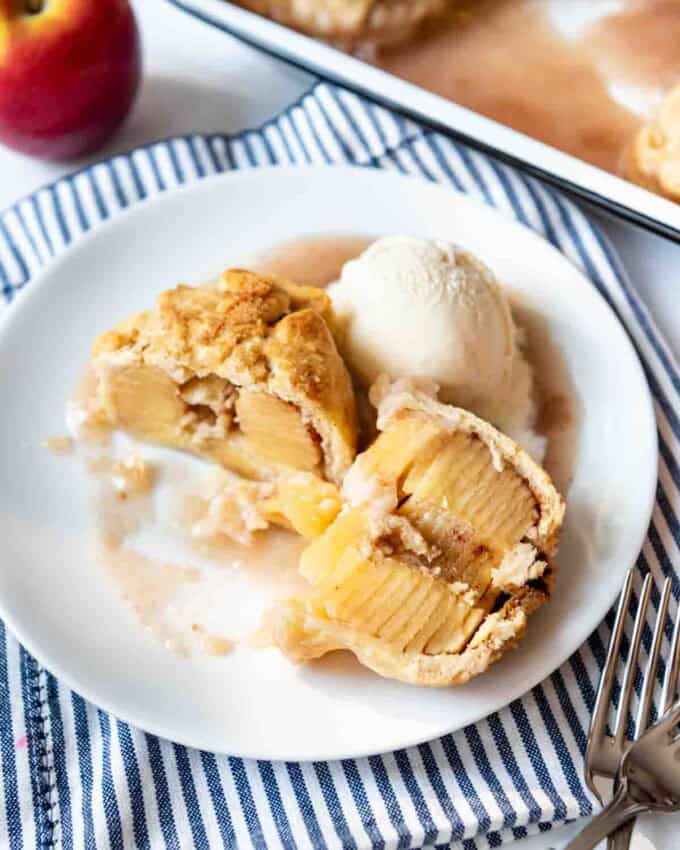 An apple dumpling sliced open on a white dessert plate with a scoop of ice cream.