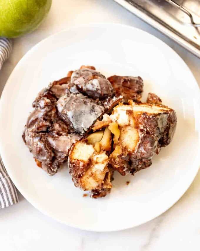 A torn apart apple fritter on a white plate.