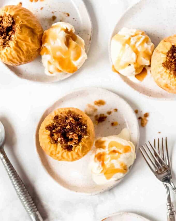 An overhead image of baked apples on plates with ice cream and caramel sauce.