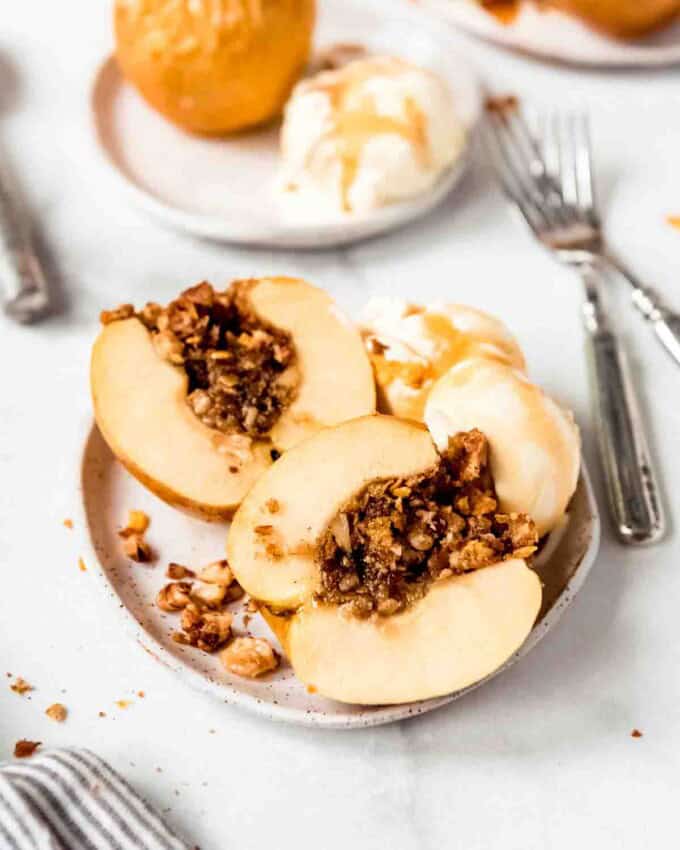 A baked apple that has been cut in half on a plate with ice cream, with more baked apples in the background.