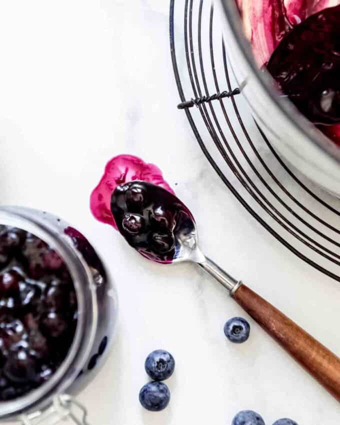 A spoonful of blueberry pie filling beside a pot of pie filling cooling on a wire rack.